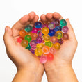 Load image into Gallery viewer, A child's hands holding a large handful of expanded, colorful Zanny Marbles water beads, demonstrating sensory exploration and fine motor skills.
