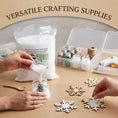 Load image into Gallery viewer, Crafting workspace with artificial snow bag, funnel, wooden snowflakes, glitter jars, and glue gun for DIY winter holiday projects.
